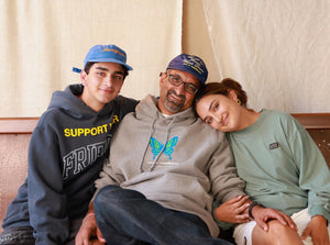 Two men wearing Kids Of Immigrants hoodies and hats and woman wearing spread love 2.0 tee